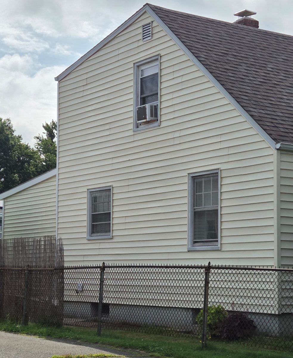 After: The same house finished in new cream vinyl siding with clean trim around the windows